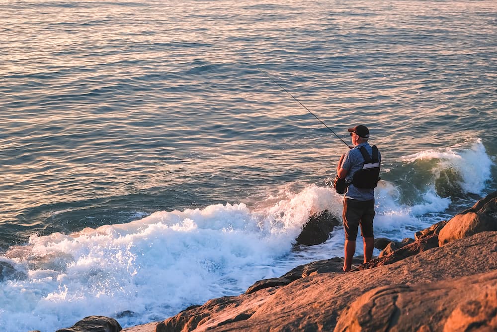 Man fishing on the west coast, standing on rocks.